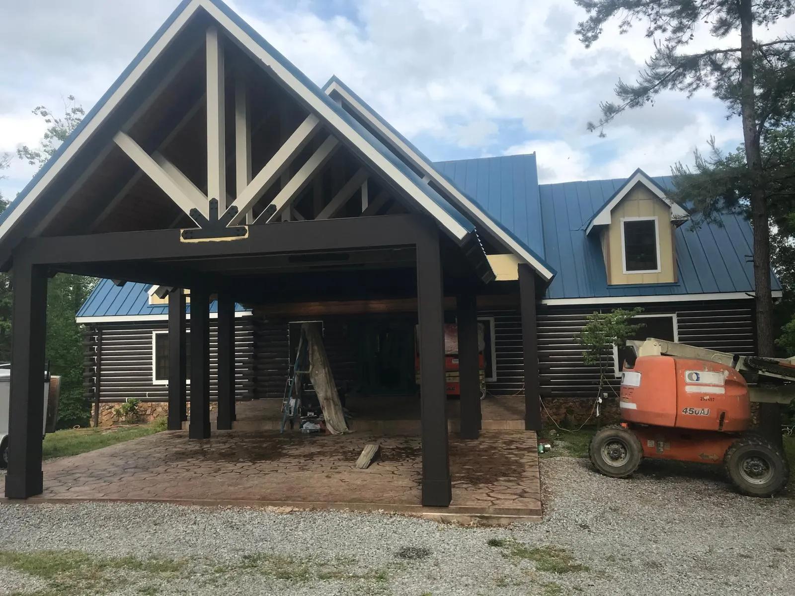 Freshly stained log home with timber-frame pavilion and boom lift on site
