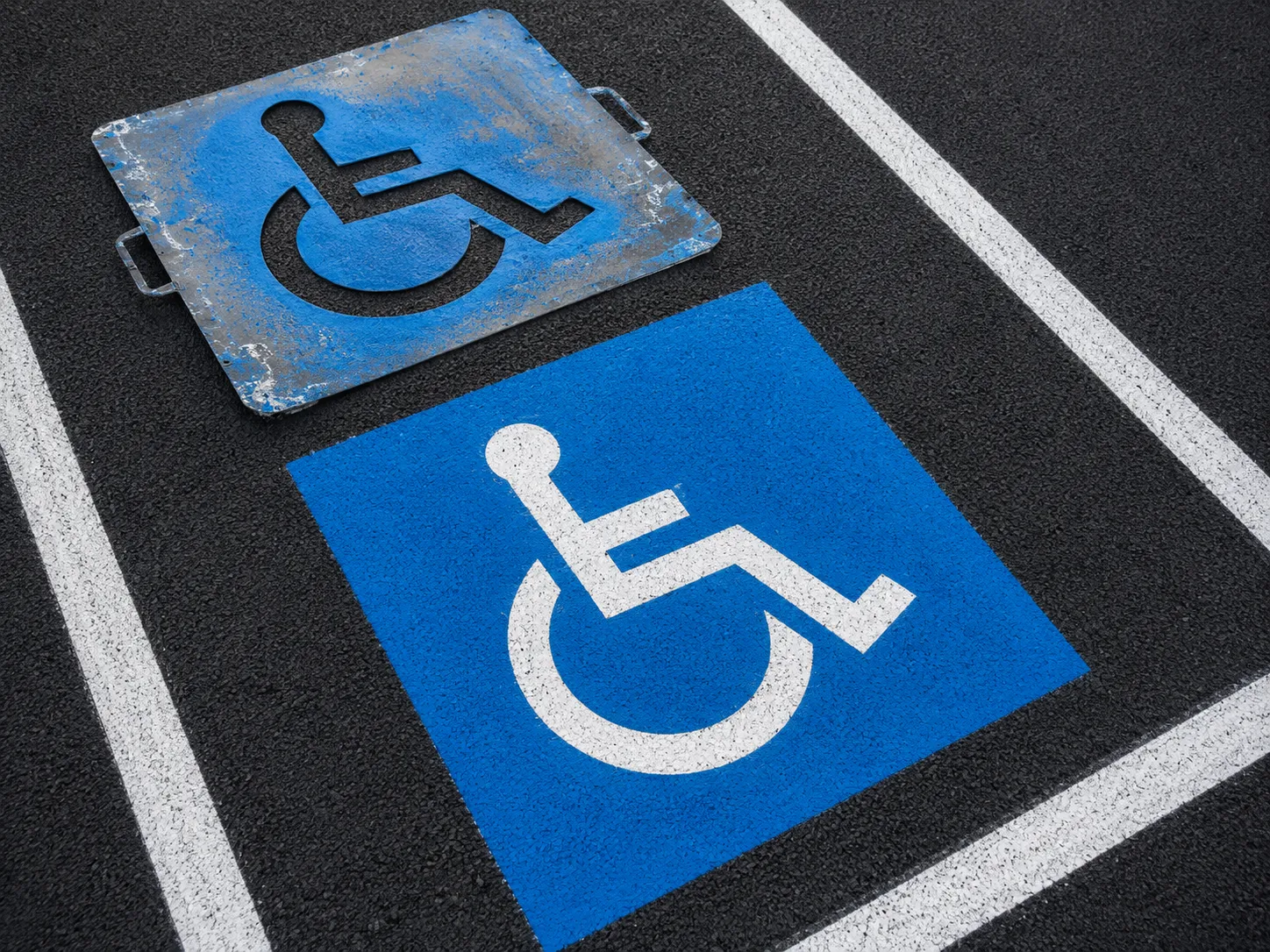 Freshly sprayed blue ADA accessible parking symbol with stencil resting beside it